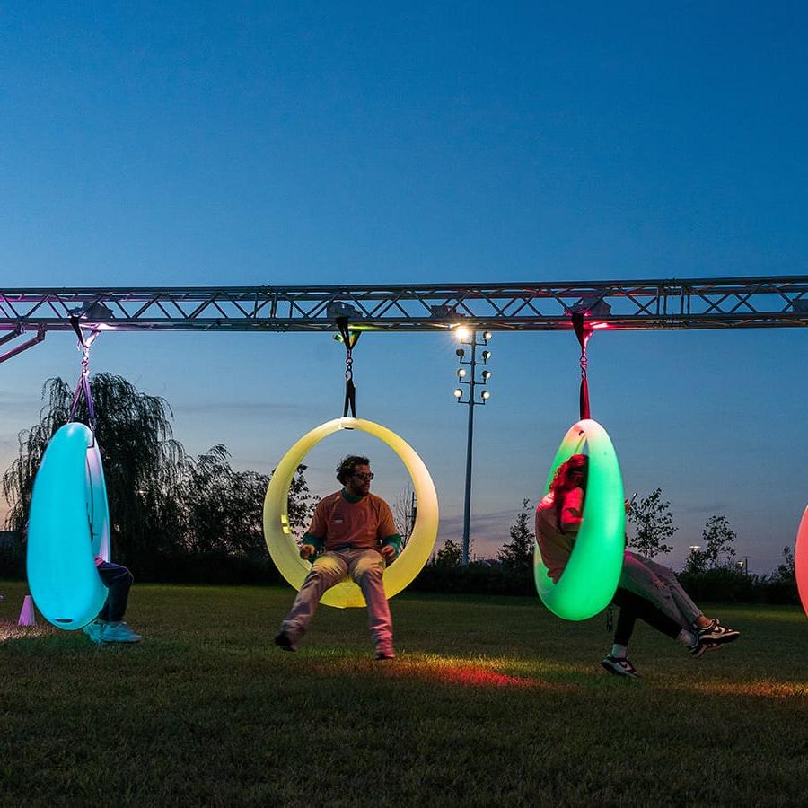 Students in neon circle swings on campus center lawn.