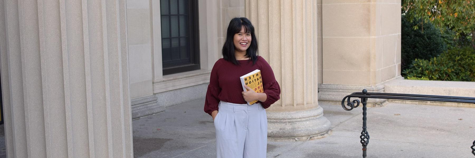 Graduate student in Conflict Resolution holds book on steps of a courthouse.